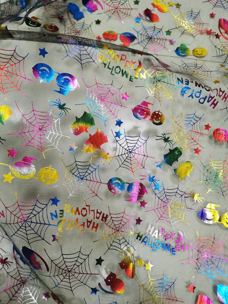 K&ouml;nnte beinhalten: Regenbogenfarbener, schimmernder Stoff mit einem schwarzen Netz&uuml;berzug. Der Stoff zeigt ein sich wiederholendes Muster aus Spinnweben, Sternen und dem Text "Happy Halloween".