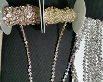 Peut inclure: Trois bobines de galon en strass, une en or rose, une en or et une en argent. Chaque bobine est enroulée d'une chaîne de petits strass transparents.