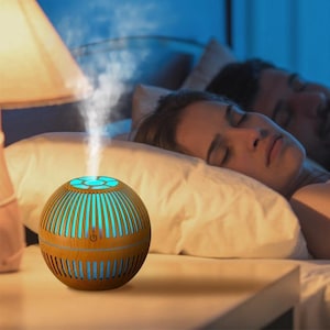 May include: A spherical essential oil diffuser with a light brown wood grain finish and vertical slats. The device emits a steady stream of mist from the top and features a glowing turquoise light visible through the slats, with a power button icon.