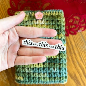 May include: A green and yellow crocheted pouch with a pink flower embellishment. A sticker with the text "this and this and this" is attached to the pouch.