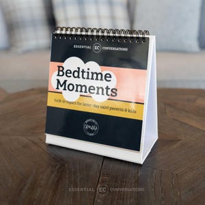 May include: A black and white spiral bound book with a pink and white cloud design. The book is titled "Bedtime Moments" and says "tuck-in topics for latter-day saint parents & kids".