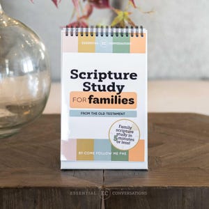 May include: A white spiral-bound "Scripture Study for Families" book with text in black and orange. The book includes the text "From the Old Testament" and "Family scripture study in 5 minutes or less!" on a wooden surface.