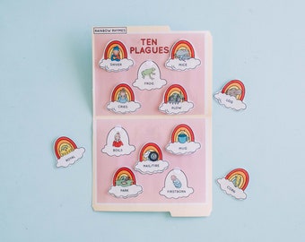 Puede incluir: Una carpeta rosa con un diseño de arcoíris y las palabras "RAINBOW RHYMES" y "TEN PLAGUES". La carpeta contiene tarjetas coloridas en forma de arcoíris con ilustraciones y palabras relacionadas con las diez plagas de Egipto.