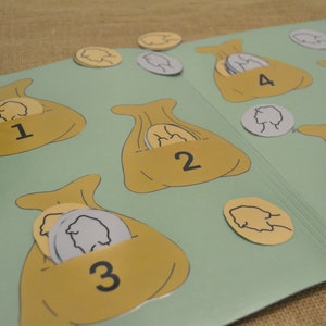 May include: A green felt board game with six brown bags with numbers 1 through 6 on them. Each bag has a different number of gold coins with a profile of a person on them inside.