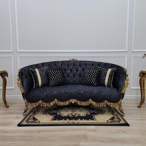 May include: A luxurious navy blue sofa with gold trim and matching pillows. Two ornate side tables with marble tops and a rug with a floral design complete the elegant living room setting. A horse statue is on one table.