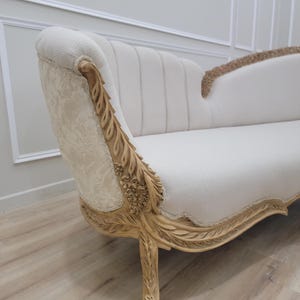Pu&ograve; includere: Un divano in tessuto bianco con gambe in legno intagliate ornate e uno schienale curvo. Il divano ha una finitura in legno chiaro e dettagli intricati.