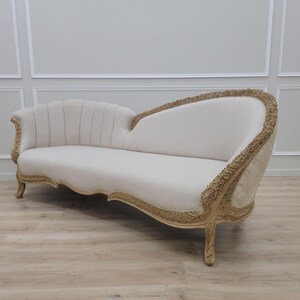 Pu&ograve; includere: Una chaise longue bianca, riccamente intagliata, con rivestimento in tessuto bianco. La chaise longue ha uno schienale curvo e un fronte a conchiglia. Le gambe sono intagliate e dipinte in oro.