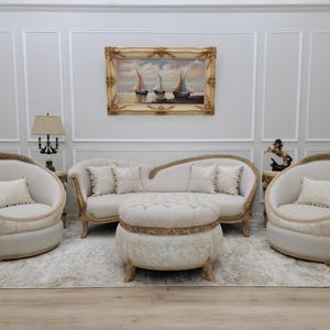 Pu&ograve; includere: Un set da salotto bianco con un divano curvo, due poltrone e un pouf rotondo. I mobili sono rivestiti in tessuto bianco con dettagli dorati. Il divano ha tre cuscini e le poltrone hanno un cuscino ciascuna. Il pouf ha un bordo dorato attorno alla parte superiore. La stanza &egrave; decorata con un dipinto di barche a vela e una lampada su un tavolino.