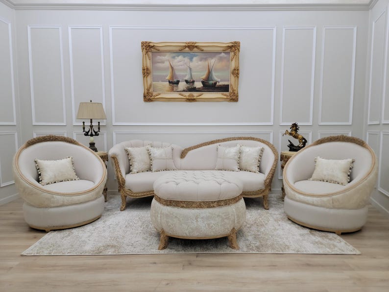 Pu&ograve; includere: Un set da salotto bianco con un divano curvo, due poltrone e un pouf rotondo. I mobili sono rivestiti in tessuto bianco con dettagli dorati. Il divano ha tre cuscini e le poltrone hanno un cuscino ciascuna. Il pouf ha un bordo dorato attorno alla parte superiore. La stanza &egrave; decorata con un dipinto di barche a vela e una lampada su un tavolino.