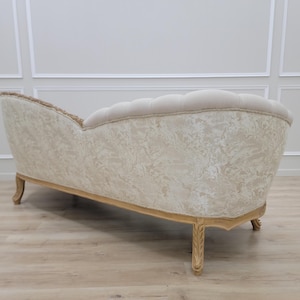 Pu&ograve; includere: Una chaise longue capitonn&eacute; bianca con un motivo floreale sul tessuto. La chaise longue ha uno schienale curvo e gambe in legno con una finitura dorata.