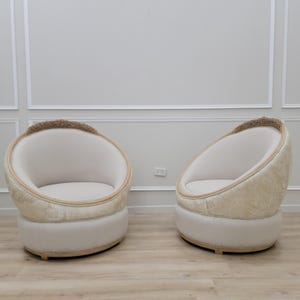 Pu&ograve; includere: Due poltrone imbottite bianche e beige con un design arrotondato a forma di uovo. Le poltrone hanno una base in legno e un rivestimento in tessuto trapuntato.