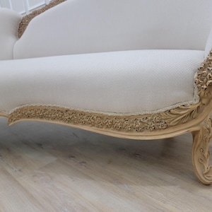 Pu&ograve; includere: Un divano in tessuto bianco con una struttura in legno intagliato. Il divano ha uno schienale curvo e dettagli decorativi. Il divano &egrave; appoggiato su un pavimento in legno chiaro.
