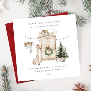 May include: A Christmas card with a red envelope. The card features a watercolor illustration of a giraffe, a Christmas tree, and a wardrobe. Text reads "HAPPY FIRST CHRISTMAS to my nanny & grandad" and "with love from your little grandson HARRY JAMES WHITE."