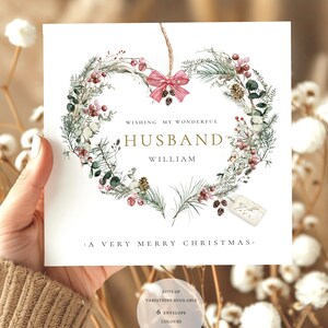 May include: A square Christmas card with a heart-shaped wreath design. The wreath is made of green and red foliage, with a red bow at the top. Text reads "Wishing My Wonderful Husband William" and "A Very Merry Christmas."