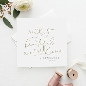 May include: A white card with gold calligraphy that reads "Will you be my beautiful maid of honour? Penelope 12.08.2020".