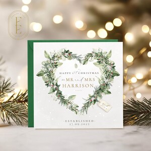 May include: A Christmas card with a green border and envelope. The card features a heart-shaped wreath of green leaves and white flowers. Text reads "Happy 1st Christmas as Mr and Mrs Harrison" and "Established 27.09.2025".