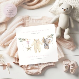 May include: A baby shower greeting card with a watercolor illustration of baby clothes and an elephant hanging on a clothesline. The card reads "To a very special mummy to be Willow" and "On your baby shower 21st December 2025". The card is surrounded by baby clothes and a teddy bear.