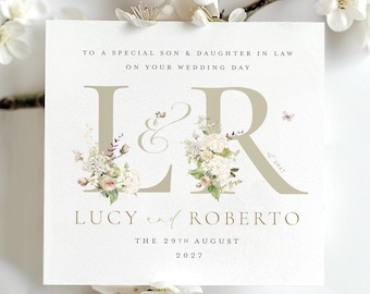 May include: A wedding card featuring the initials "L&R" in a muted tone, adorned with floral arrangements. The card's text includes "To a special son & daughter in law", the names "Lucy and Roberto", and the date "29th August 2027".
