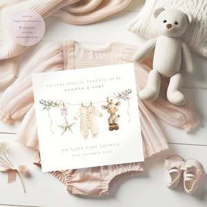 May include: A baby shower card with the text "TO VERY SPECIAL PARENTS TO BE HANNAH & TOBY ON YOUR BABY SHOWER 12TH NOVEMBER 2026". The card features illustrations of baby clothes, a star, and a giraffe. A plush teddy bear, baby shoes, and a baby outfit are also visible.