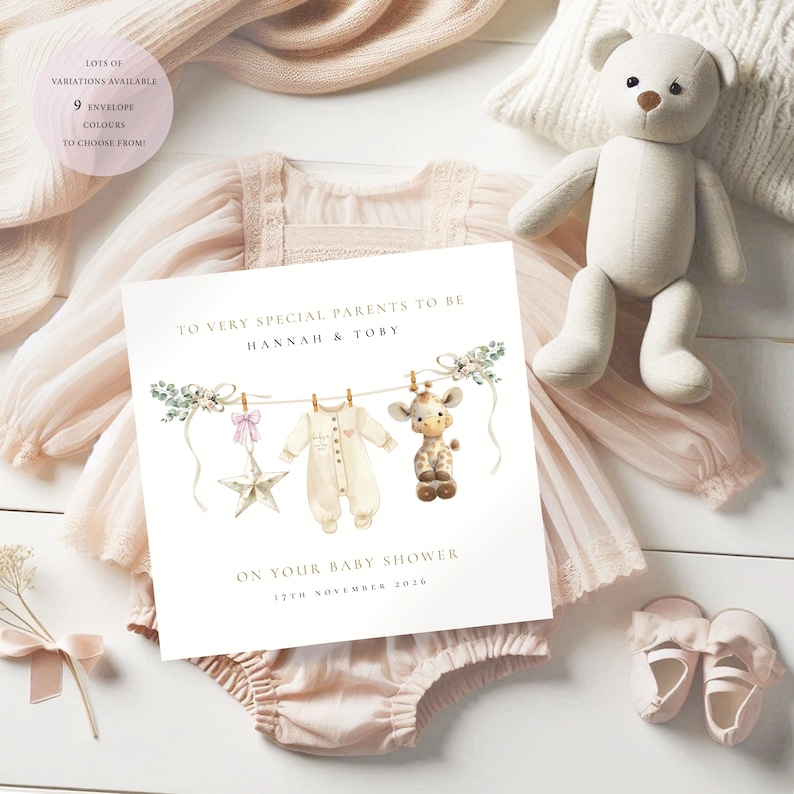 May include: A baby shower card with the text "TO VERY SPECIAL PARENTS TO BE HANNAH & TOBY ON YOUR BABY SHOWER 12TH NOVEMBER 2026". The card features illustrations of baby clothes, a star, and a giraffe. A plush teddy bear, baby shoes, and a baby outfit are also visible.