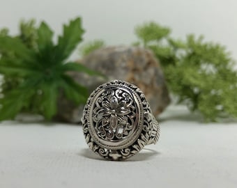 May include: A silver ring with an ornate floral design. The ring is oval shaped and has a detailed filigree pattern.