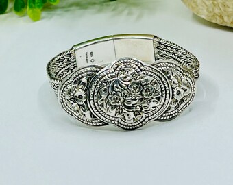 May include: A silver bracelet with a chain link design and three decorative floral medallions. The bracelet has a magnetic clasp.