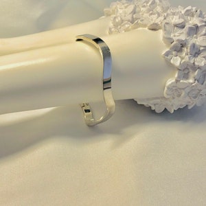 May include: A silver metal bangle bracelet with a curved design.