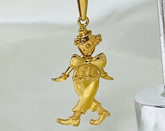 May include: A gold-toned pendant charm in the shape of a walking clown. The clown is wearing a hat, a bow tie, and has a whimsical expression.