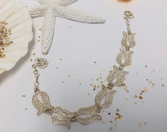 May include: A silver bracelet with a delicate filigree design featuring a series of tulip-shaped charms. The bracelet is on a white background with small white and gold flecks.