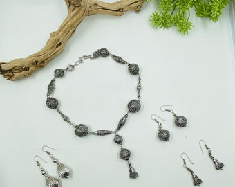 May include: A silver necklace with a pendant and matching earrings. The necklace is made of silver beads with intricate designs. The earrings are also silver and have a teardrop shape.