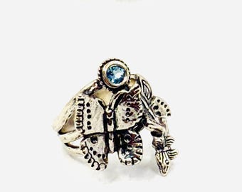 Könnte beinhalten: Silberfarbener Ring mit einem detaillierten Schmetterlingsdesign. Der Schmetterling hat offene Flügel mit kleinen Punkten und Linien. Ein runder, hellblauer Edelstein ist oben auf dem Ring eingesetzt und setzt einen Farbakzent.