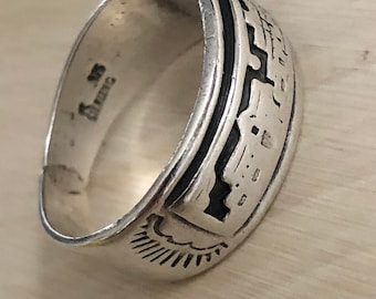 May include: A silver ring with a black inlay design. The ring features a stylized image of a building with a sunburst design on the bottom. The ring is marked "STERLING" on the inside.