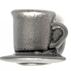 May include: A silver-toned metal teacup and saucer. The cup has a rounded handle and a slightly flared rim. The saucer is round and has a slightly raised edge.