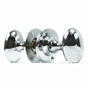 May include: A pair of polished chrome door knobs with an oval shape. The knobs are attached to a round base with screws.