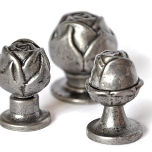 May include: Three silver-toned metal rose bud drawer pulls. The pulls are different sizes and have a detailed rose bud design.