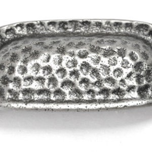 May include: A silver-toned, hammered metal drawer pull with a rounded, oval shape. The pull has a smooth, textured surface and two small screws on either side.
