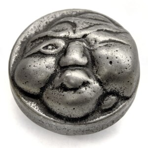 May include: A silver-toned metal knob with a detailed face sculpted into the surface. The face has a furrowed brow, a large nose, and a slightly open mouth.
