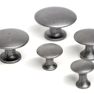 May include: Five different sizes of pewter cabinet knobs. The knobs are round and have a mushroom shape. They are all a silver colour.