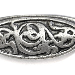 May include: A silver-toned metal drawer pull with an ornate design. The pull has a rounded oval shape with a decorative pattern in the centre. The pull has two screw holes on either side.