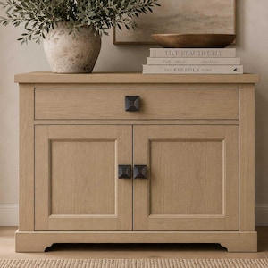 May include: A light oak wood cabinet featuring one top drawer and two lower cabinet doors. Each door and the drawer are fitted with a dark square knob. The cabinet has a rectangular frame with a flat top surface and a base with a cutout design.