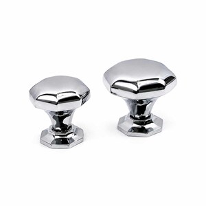 May include: Two polished chrome cabinet knobs with a faceted hexagonal top and a matching hexagonal base. The metallic surface is highly reflective, showing clear highlights and shadows on the smooth, geometric surfaces of both hardware pieces.