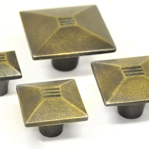 May include: Four square cabinet knobs with a distressed brass finish. The knobs have a raised square design with a recessed line pattern.
