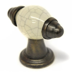 May include: A white ceramic cabinet knob with a crackled finish and antique brass accents. The knob has a rounded oval shape and a pointed end.