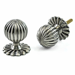 May include: Two silver door knobs with a fluted design and a decorative base. The knobs are shown from different angles.