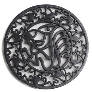 May include: Black cast iron trivet with a decorative design of leaves and acorns. The trivet is round and has a diameter of approximately 20 cm.
