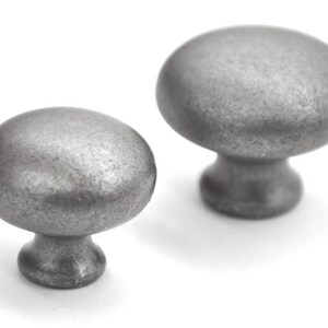 May include: Two antique-style cabinet knobs with a brushed, metallic finish. The knobs have a rounded, oval shape and a short, pedestal base. The colour is a muted, silvery grey, suitable for furniture hardware.