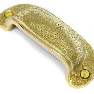 May include: A brass cabinet pull with a hammered finish. The pull has a rounded, rectangular shape with two small brass screws.