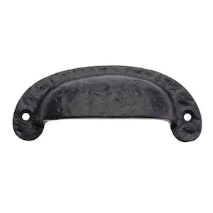 May include: Black cast iron drawer pull with a rounded, slightly curved shape. The pull has a smooth, slightly textured surface.