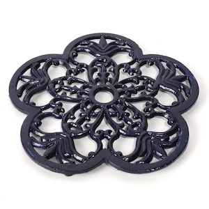 May include: A dark blue cast iron trivet shaped like a flower with intricate detailing. The trivet has a circular hole in the centre.