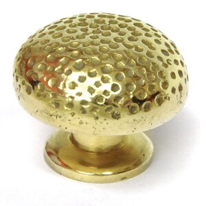 May include: A brass cabinet knob with a hammered, dimpled surface. The knob has a round top and a circular base.